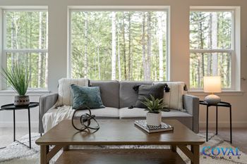 Bright living room with gray sofa, wooden coffee table, lamps, and large windows overlooking trees