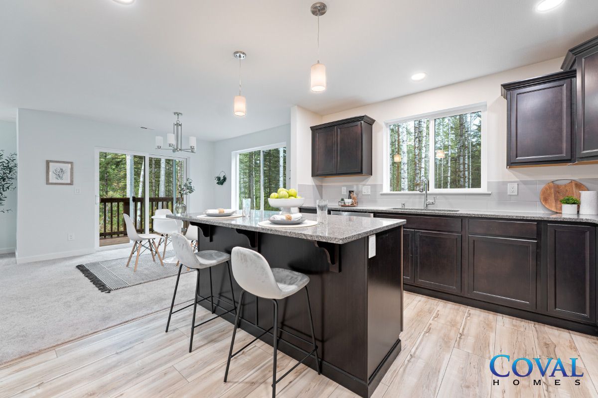 Bright modern kitchen with island, dark cabinets, white counters, and dining area by large windows