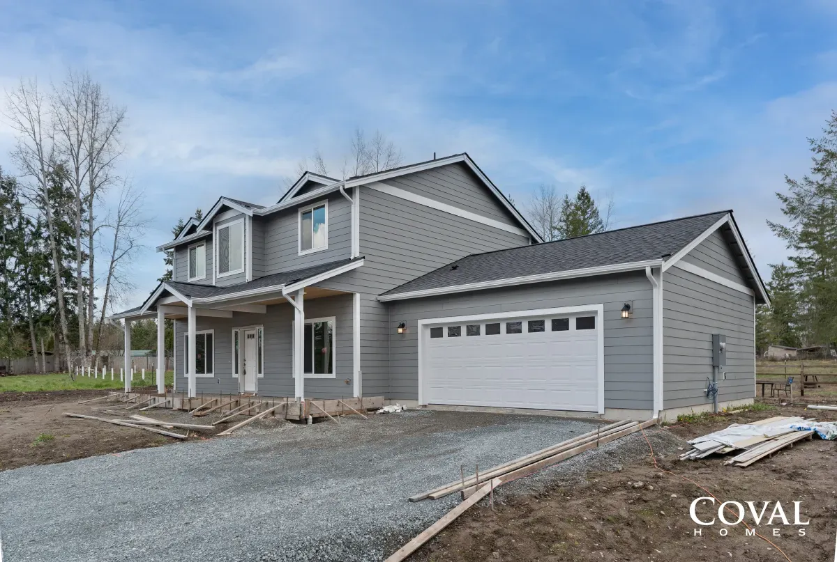 New gray two-story house with attached garage and gravel driveway under construction