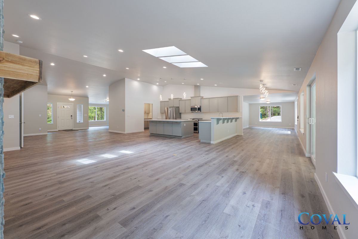 Bright open-concept kitchen and living area with light wood floors, white walls, and skylights
