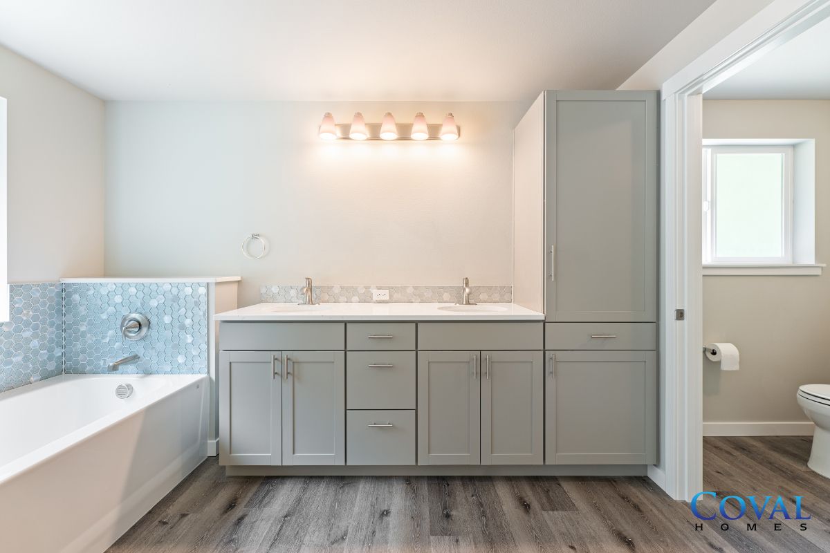 Bright modern bathroom with a bathtub, gray vanity, and large mirror with lights