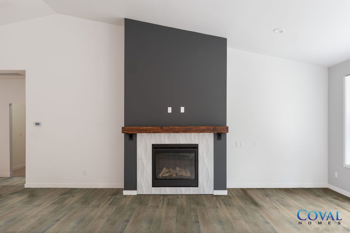 Modern living room with a black fireplace, wood mantel, and gray accent wall on wood flooring