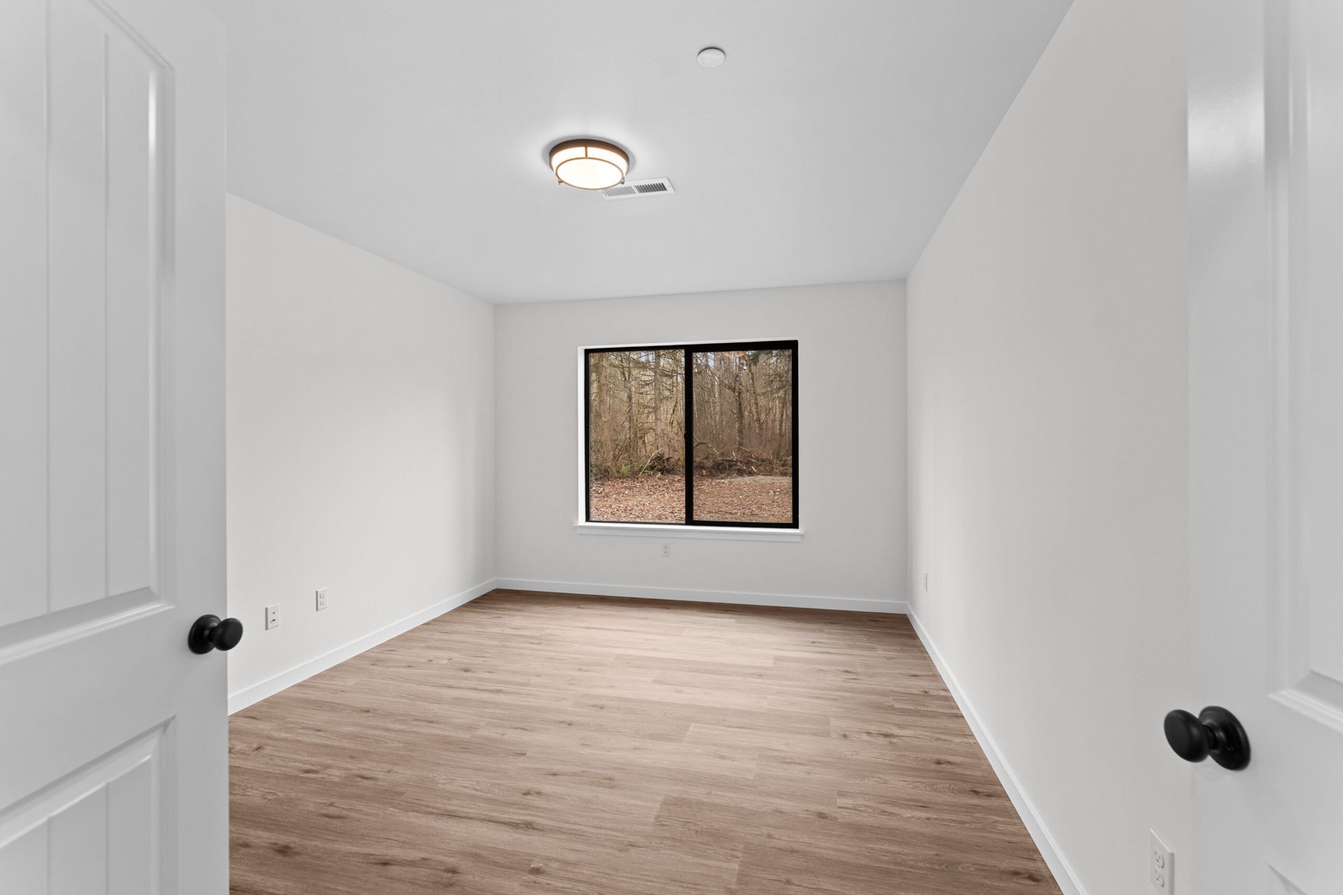 Empty white room with wood flooring, window, and open double doors