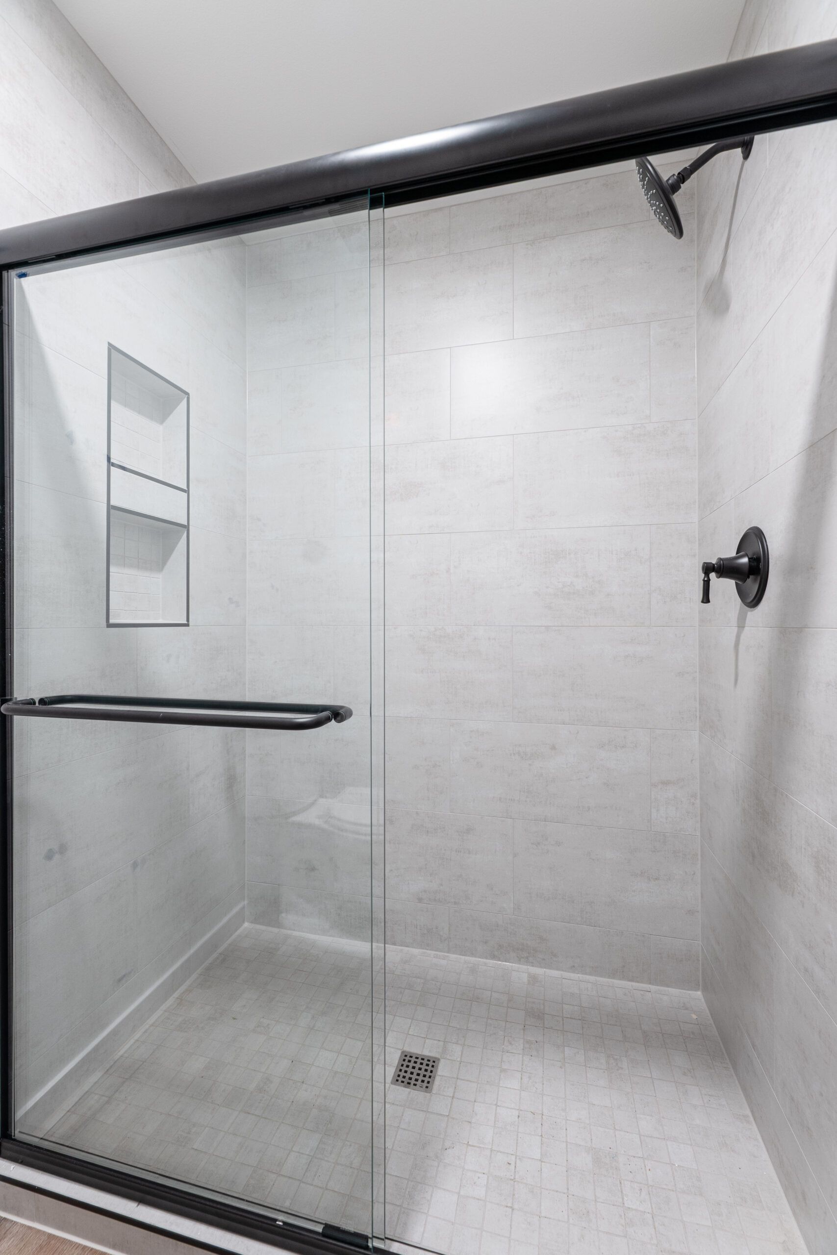 Glass-enclosed walk-in shower with white tile, black fixtures, and a wall shelf