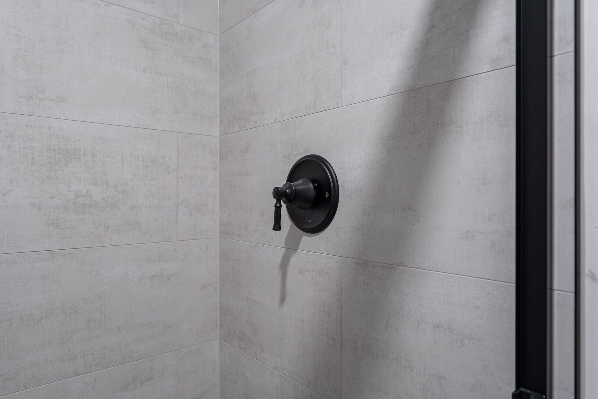 Black wall-mounted shower fixture on a light gray tiled bathroom wall.