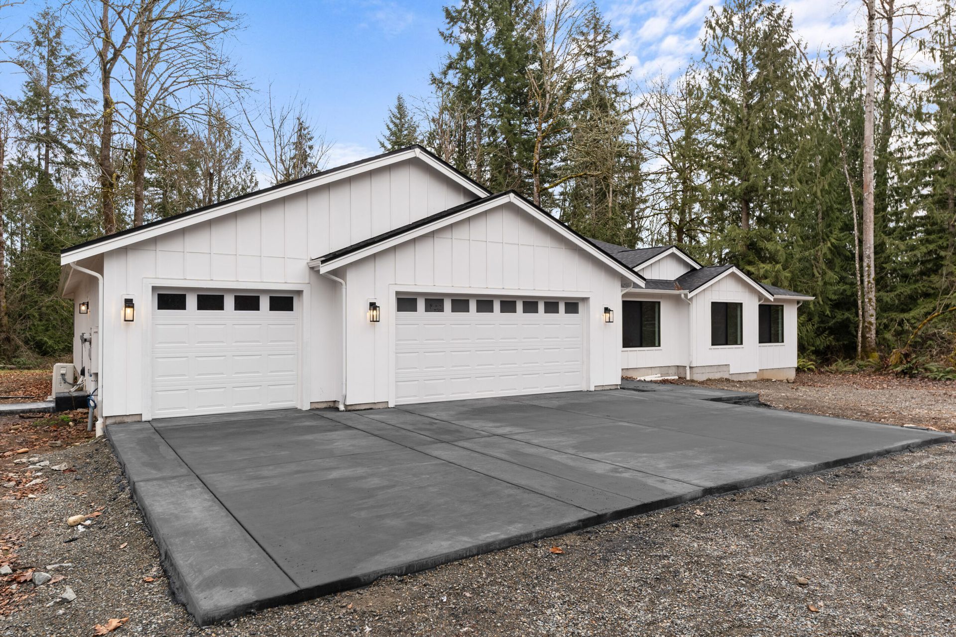White house with three garage doors and a wide paved driveway in a wooded area.