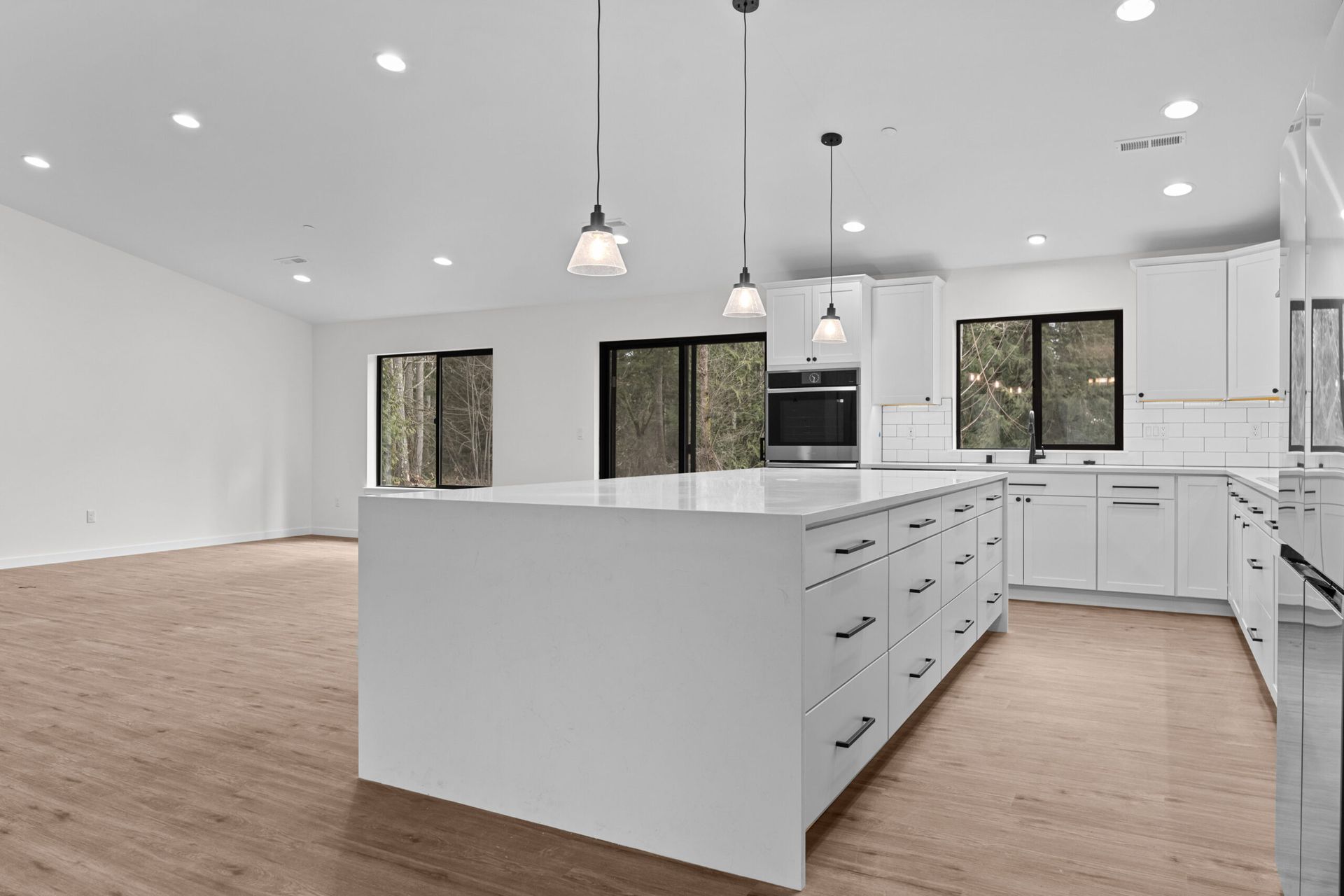 Bright modern kitchen with white cabinets, island, pendant lights, and wood flooring