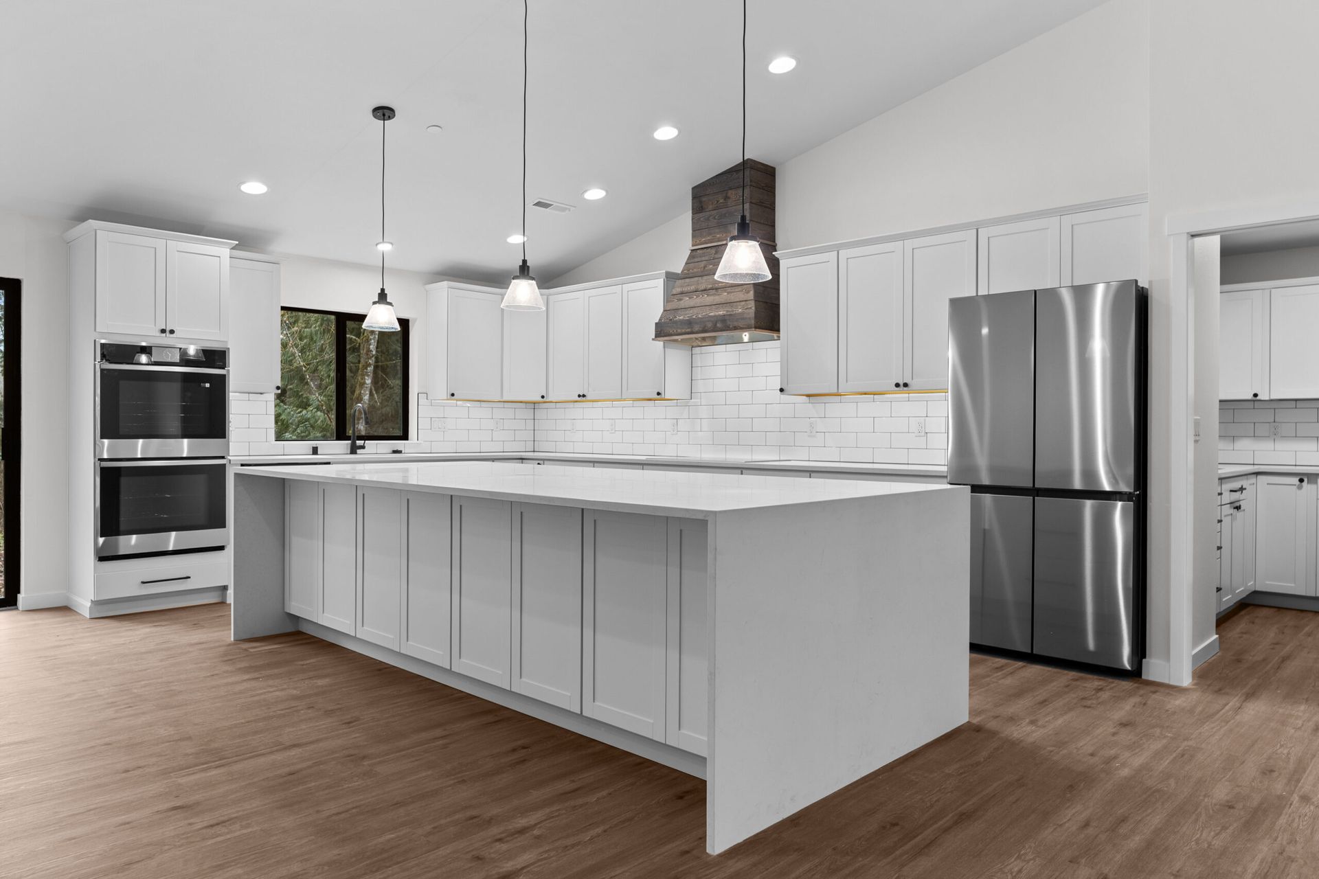 Modern white kitchen with large island, stainless steel appliances, pendant lights, and wood flooring