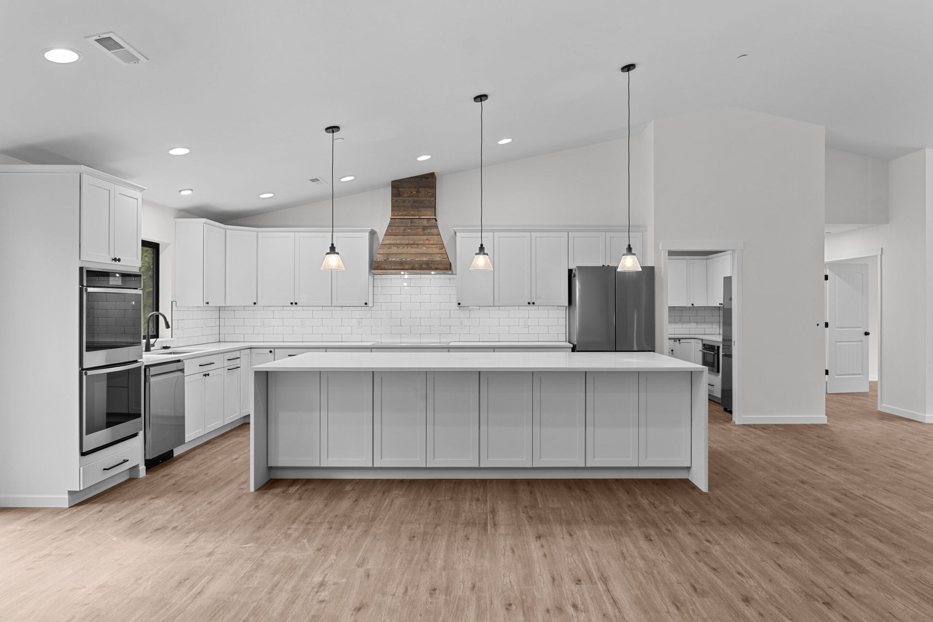Bright modern kitchen with white cabinets, large island, stainless appliances, and wood floors