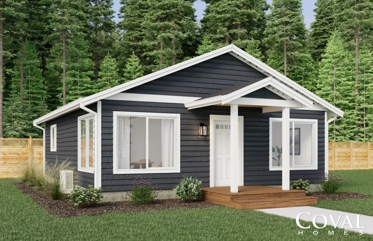 Small dark-gray modern cottage with white trim and front porch, set among tall evergreen trees.