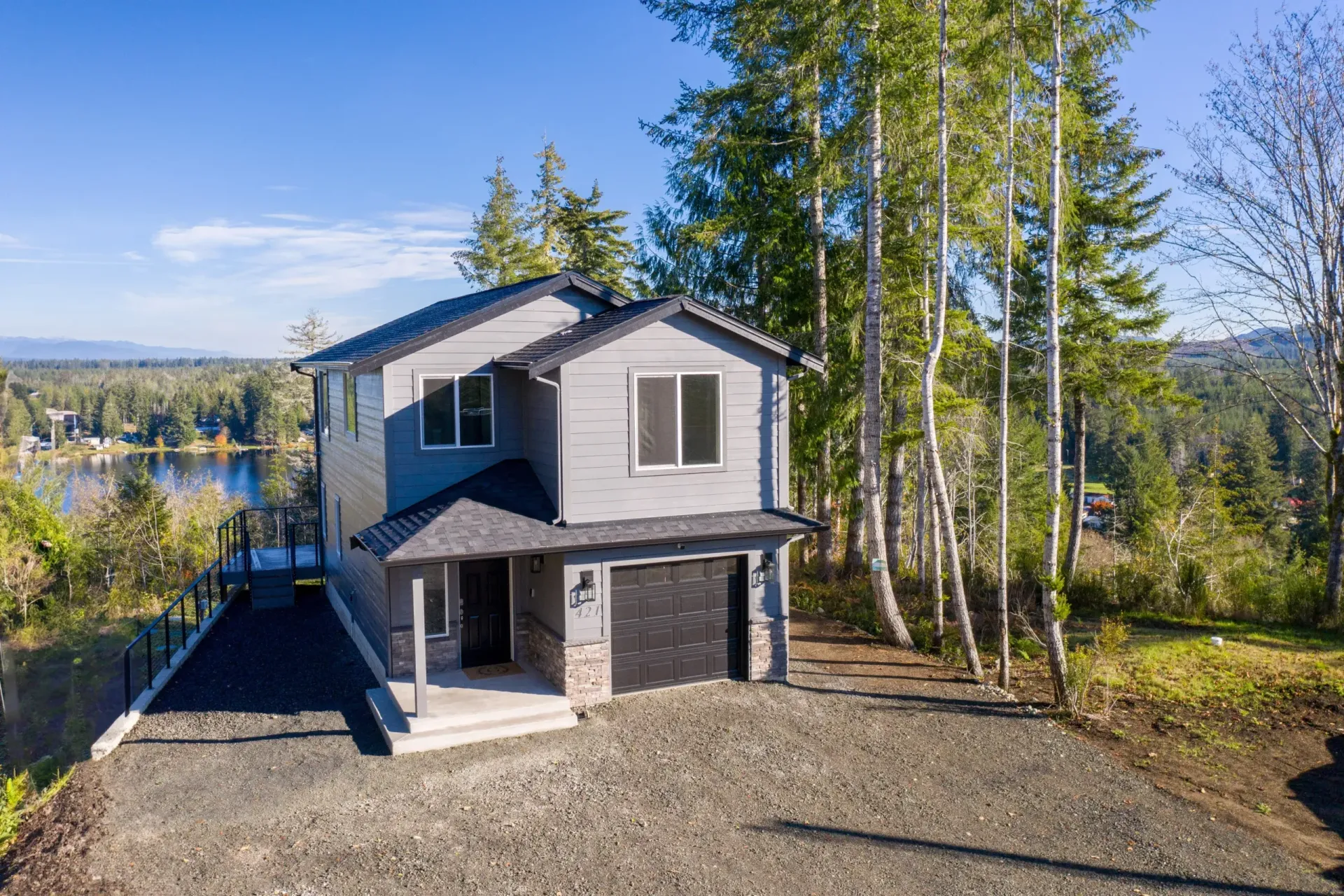 Modern two-story gray house with garage on a wooded lot under a bright blue sky