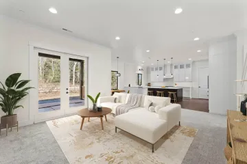 Bright modern living room with white sofa, coffee table, and open kitchen beyond French doors