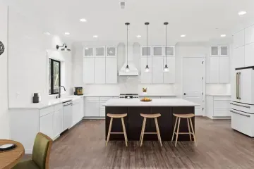 Bright white modern kitchen with island, three stools, pendant lights, and dark wood floor