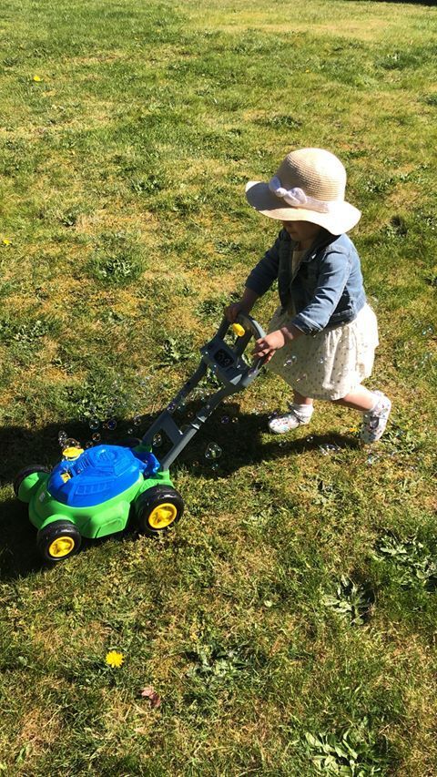 Child in a sunhat pushing a toy lawn mower across a grassy yard