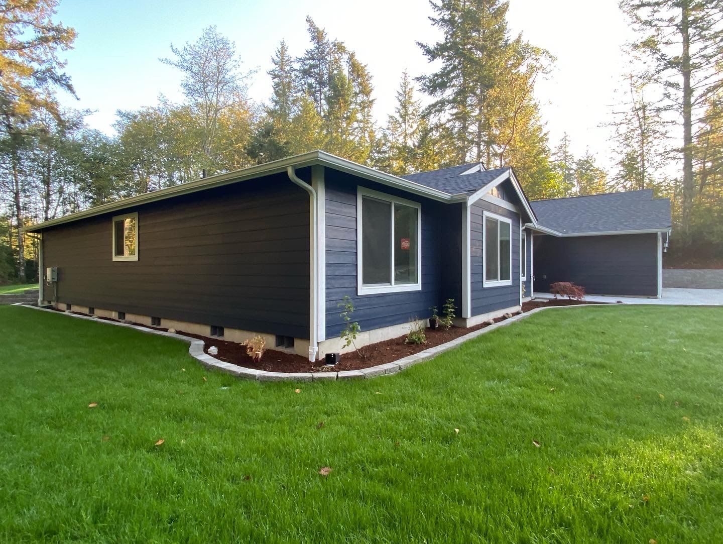 Dark blue house with white trim and attached garage on a green lawn, surrounded by trees