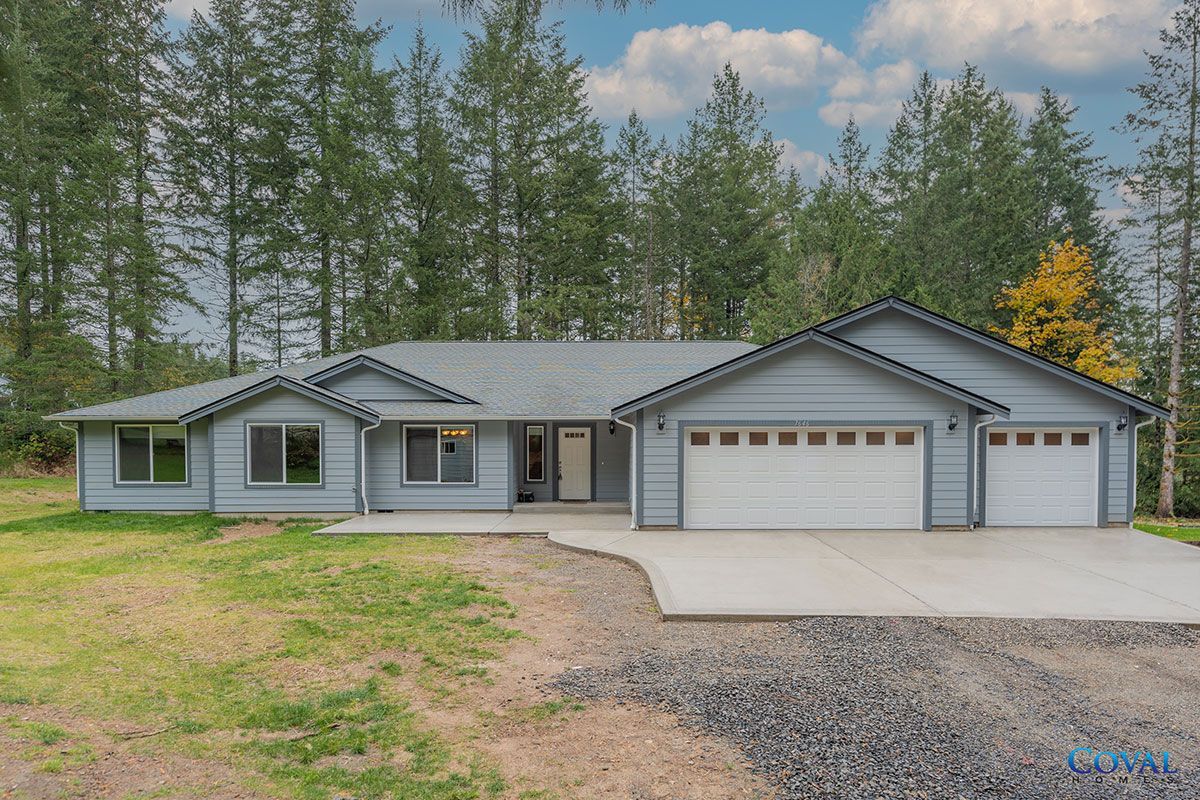 Single-story gray house with three-car garage, front driveway, and trees behind it