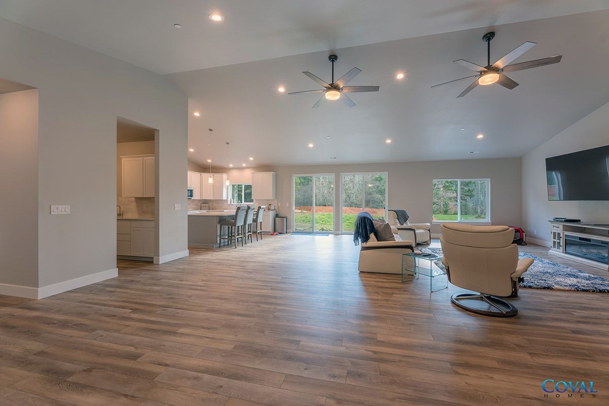 Spacious modern living room with wood floors, ceiling fans, recliner, sofa, and large windows