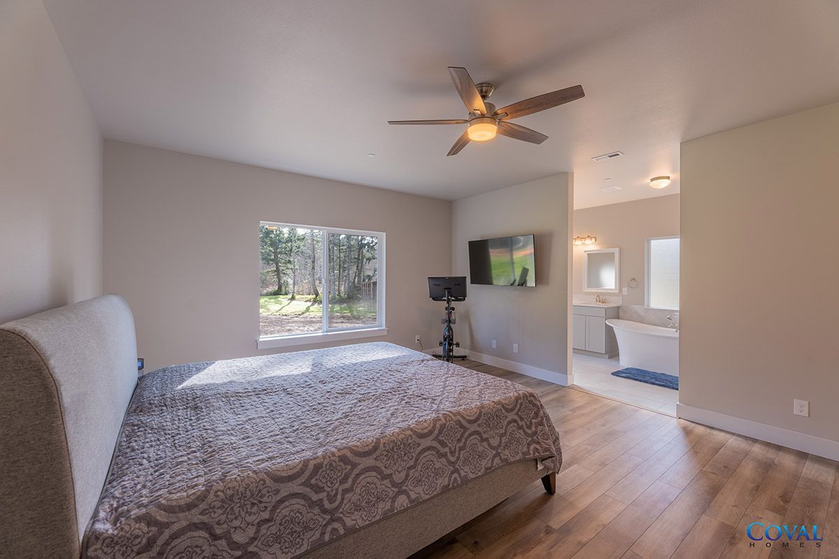 Spacious bedroom with king bed, ceiling fan, wall TV, and adjoining bathroom through an open doorway.