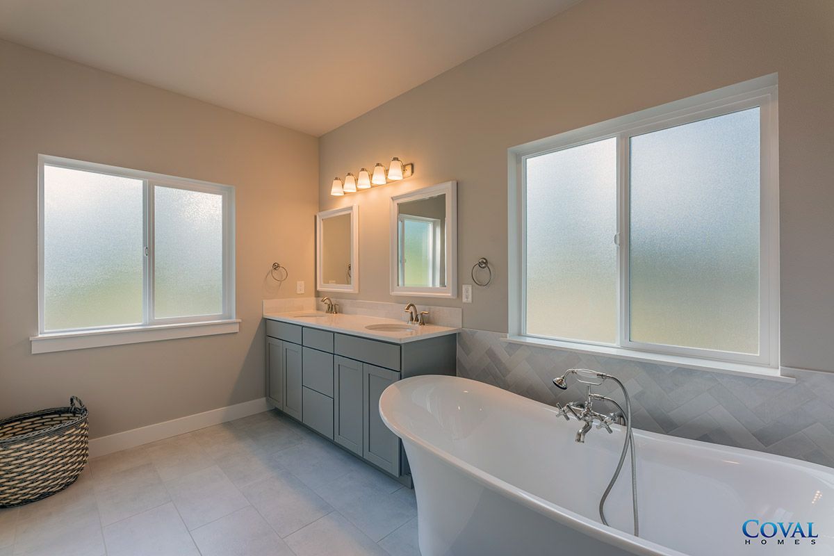 Bright bathroom with double vanity, large frosted windows, and a freestanding bathtub