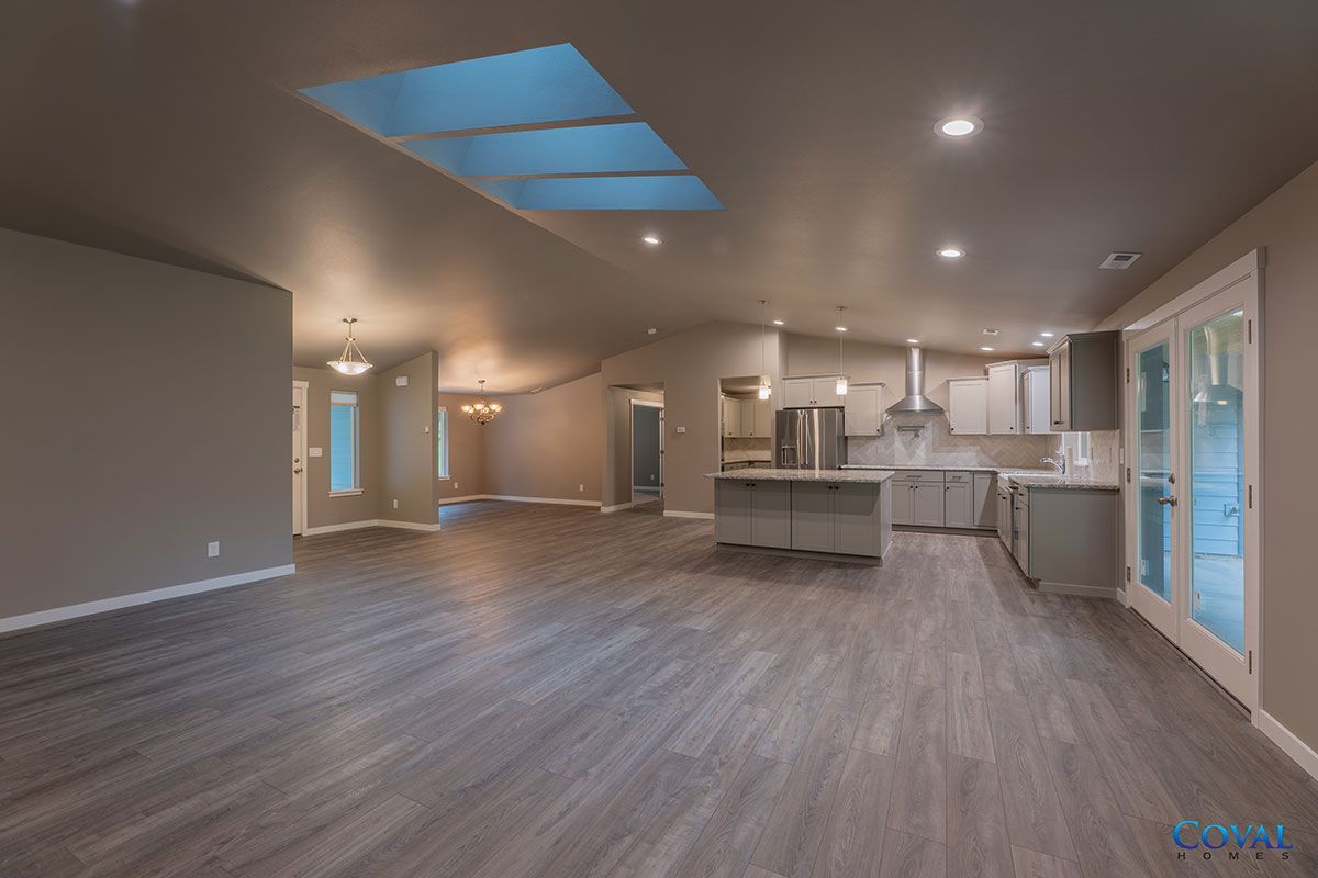 Spacious modern kitchen and living area with vaulted ceiling, skylights, gray floors, and white cabinetry