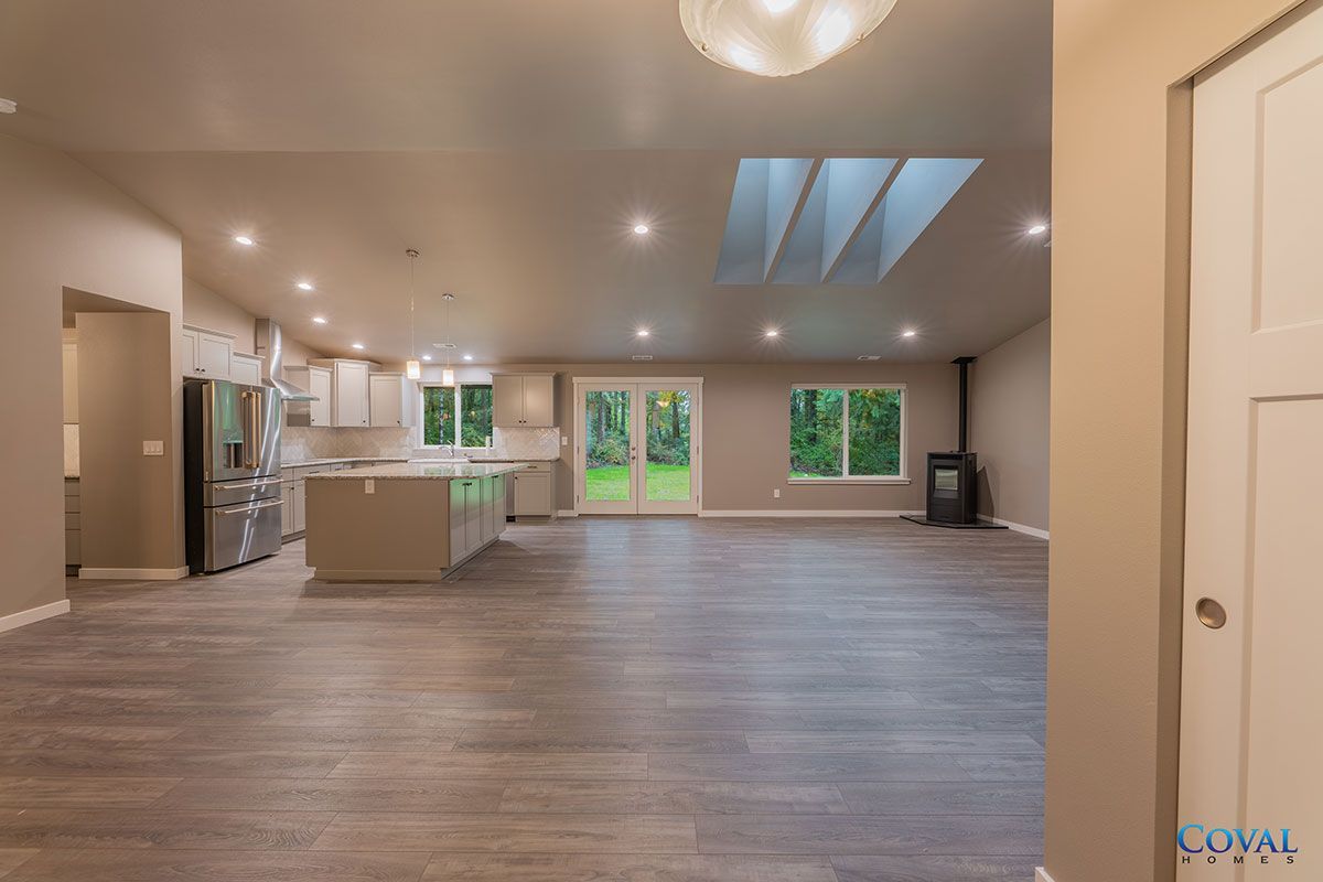 Spacious open-plan kitchen and living room with wood floors, recessed lights, skylights, and large windows.