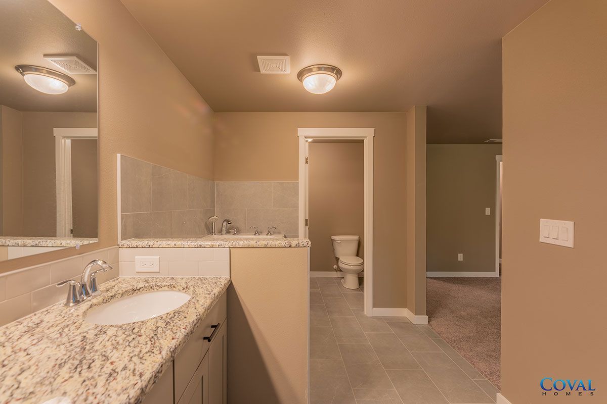 Spacious beige bathroom with double sinks, large mirror, and toilet in a separate alcove.