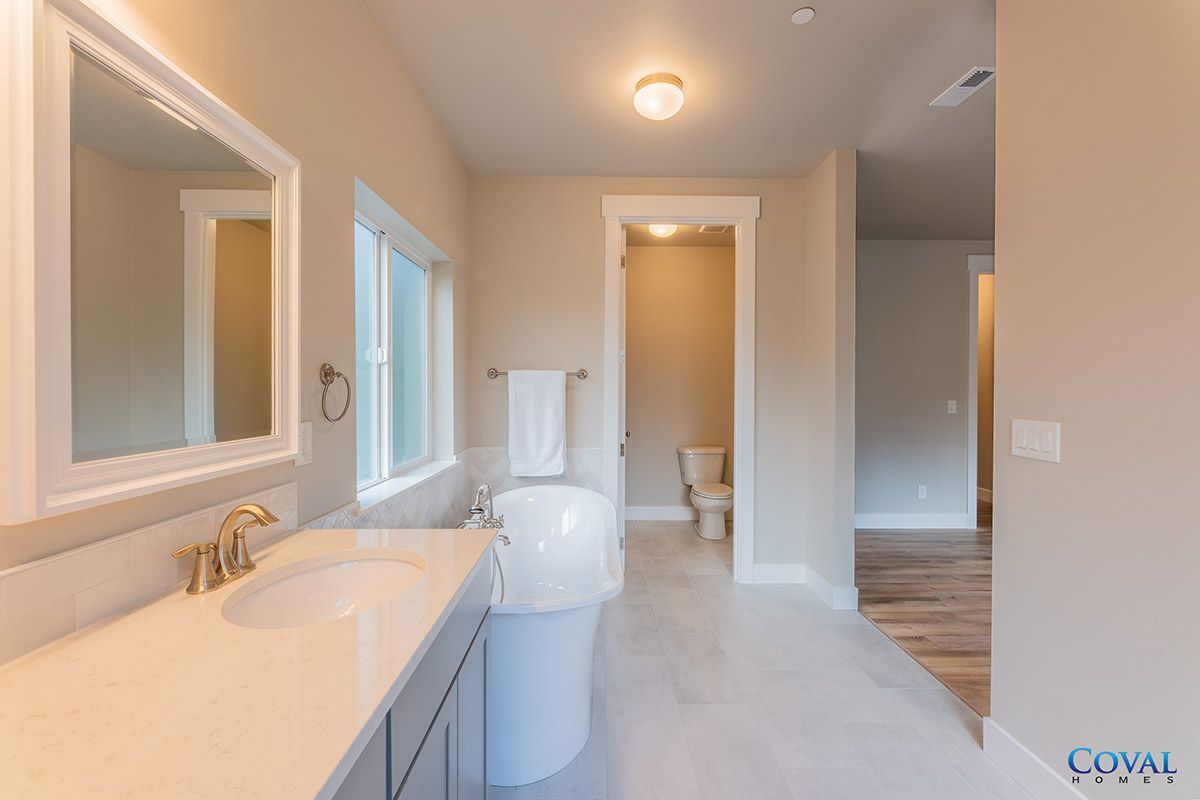 Bright bathroom with double vanity, toilet, and adjoining hallway and bedroom views