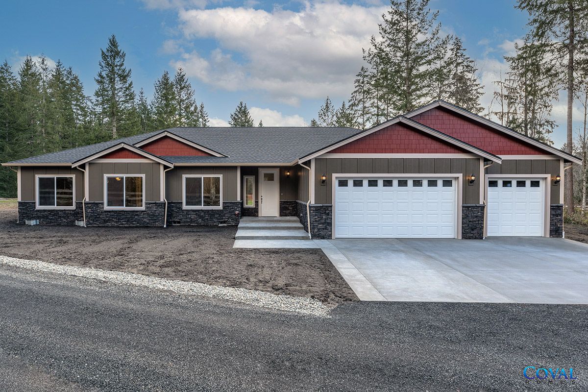 Single-story house with red roof, stone accents, and three-car garage on a gravel lot.