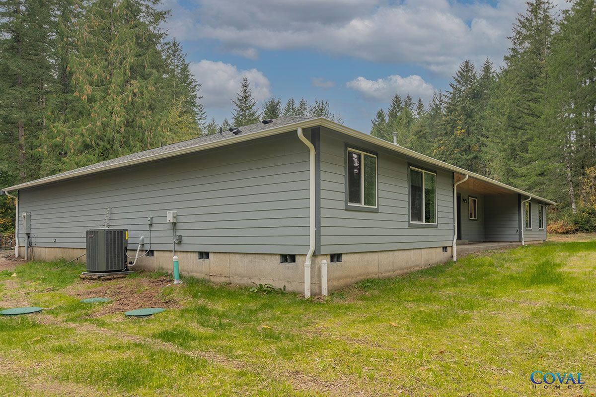 Gray cabin with green trim in a wooded area under a partly cloudy sky