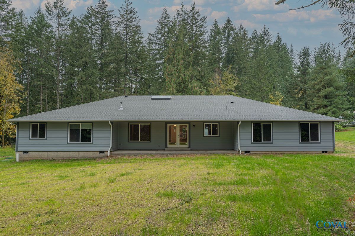 Single-story gray house with a large front lawn and tall trees in the background
