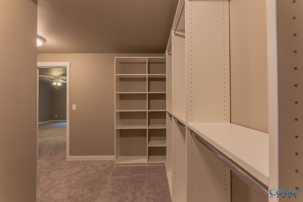 Empty walk-in closet with beige walls, carpet, and white built-in shelving units.