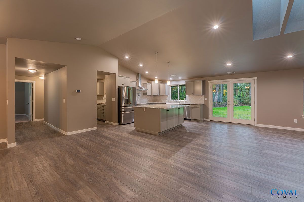 Open-concept kitchen and living area with gray floors, recessed lights, and glass doors to a green backyard.