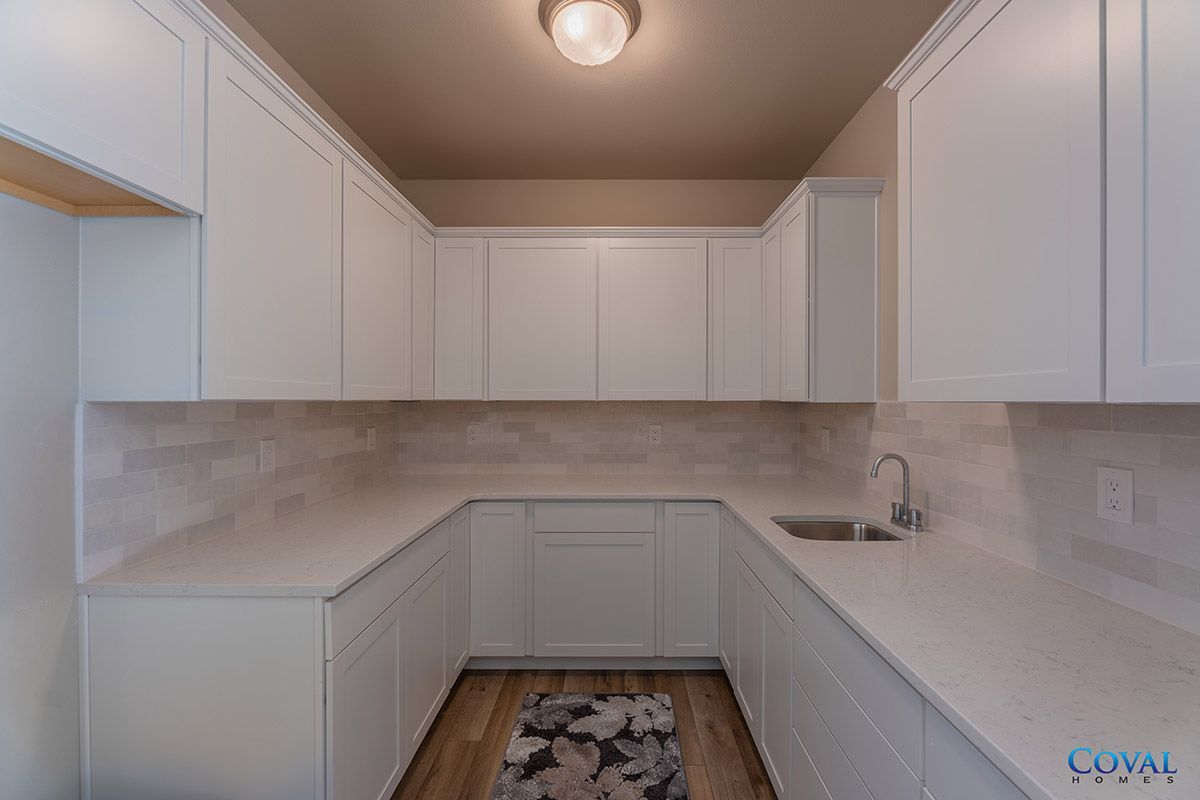 Bright white U-shaped kitchen with marble countertops, wood floor, and a ceiling light
