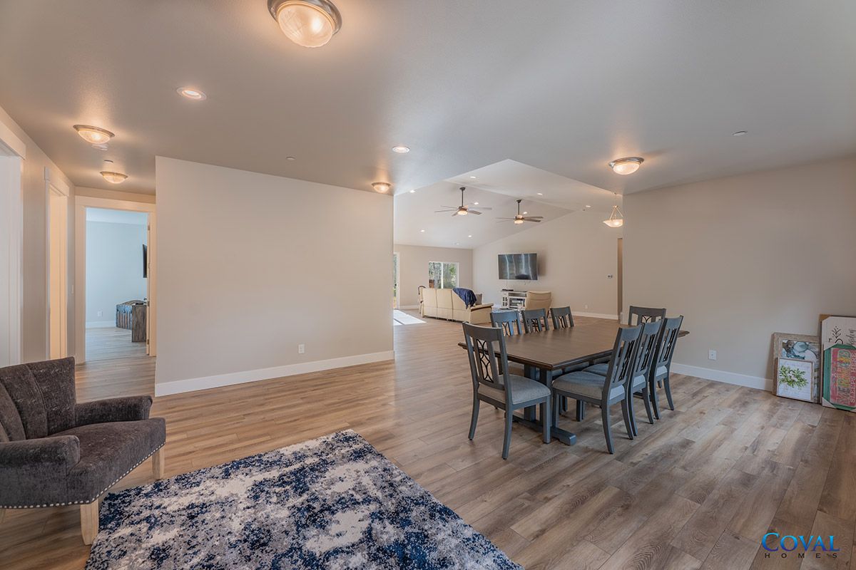 Open-concept living and dining room with hardwood floors, white walls, and a dining table near the kitchen.