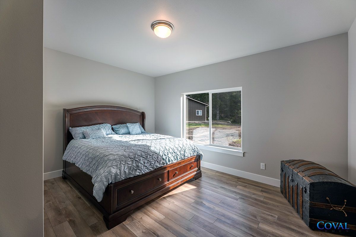 Bedroom with a dark wood bed, gray walls, window, and small storage bench on wood flooring