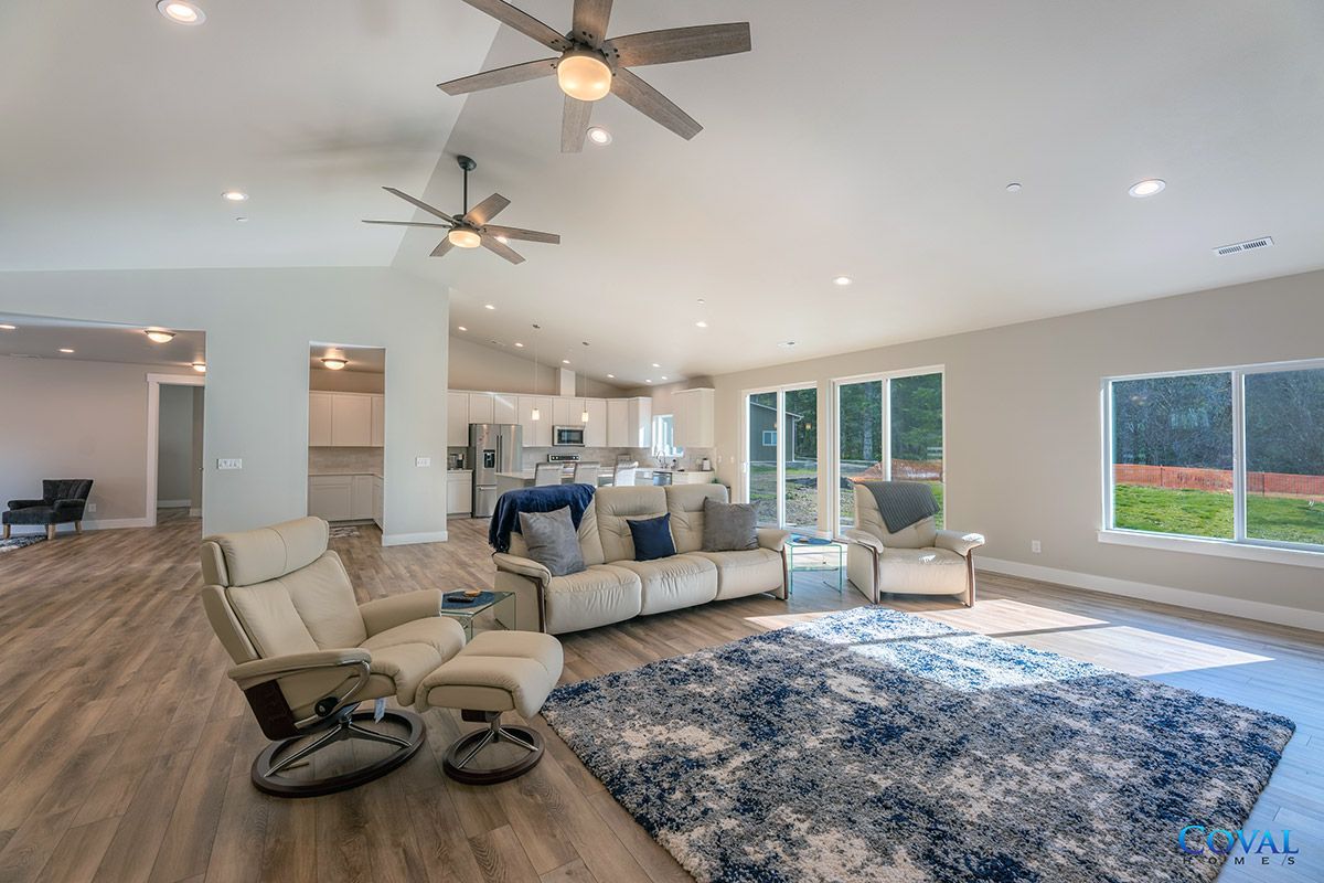 Bright open living room with recliners, sofa, blue rug, ceiling fans, and large windows overlooking a yard