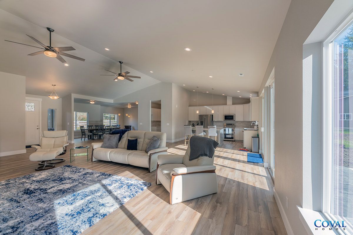 Bright open living room with beige sofas, blue rug, ceiling fans, and sunlight from large windows