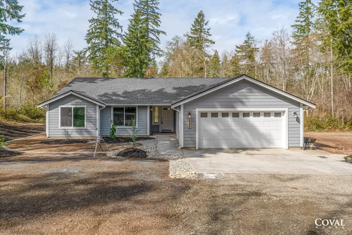 Gray single-story house with attached two-car garage and wooded yard