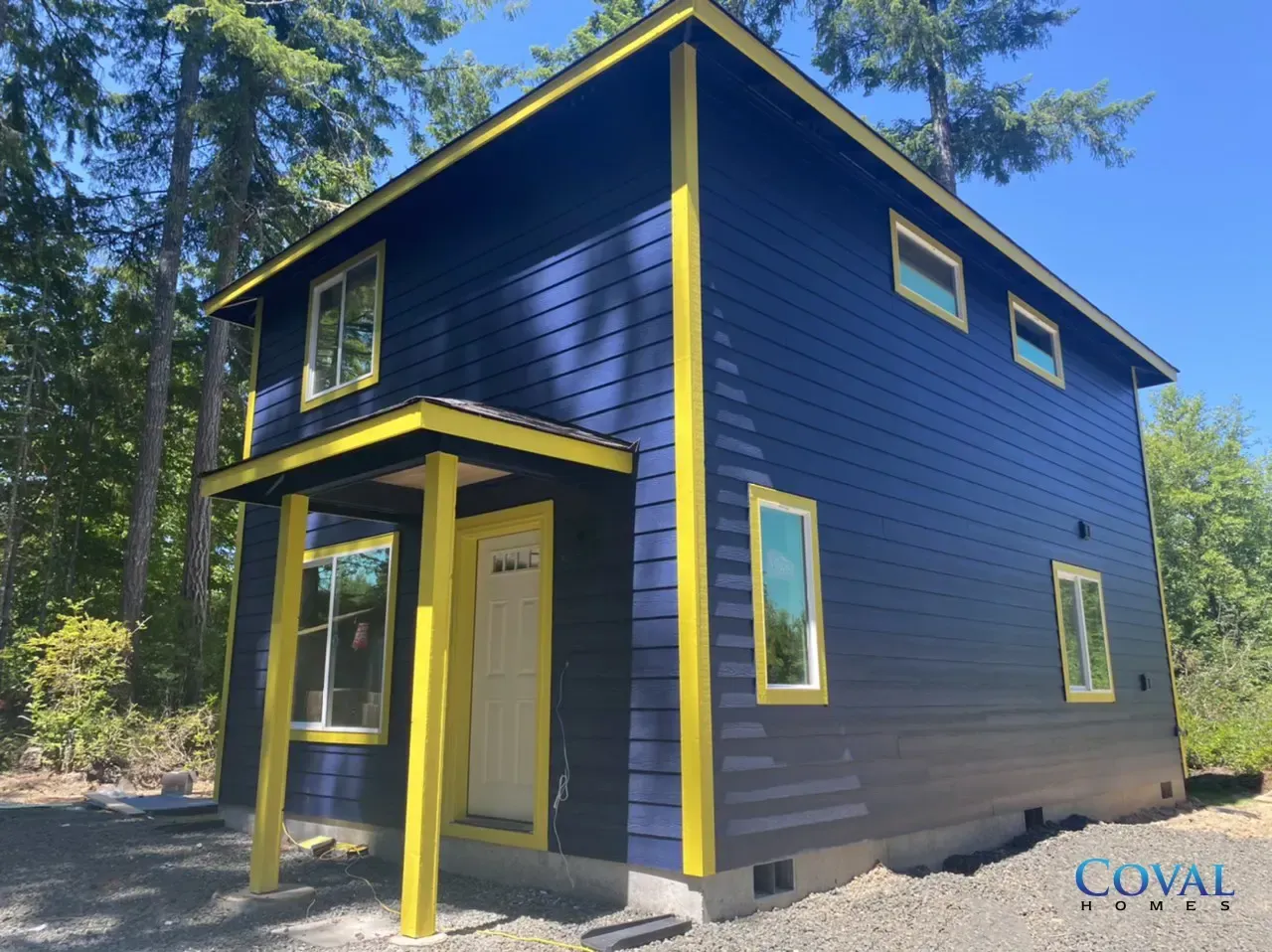 Blue two-story house with bright yellow trim in a wooded setting