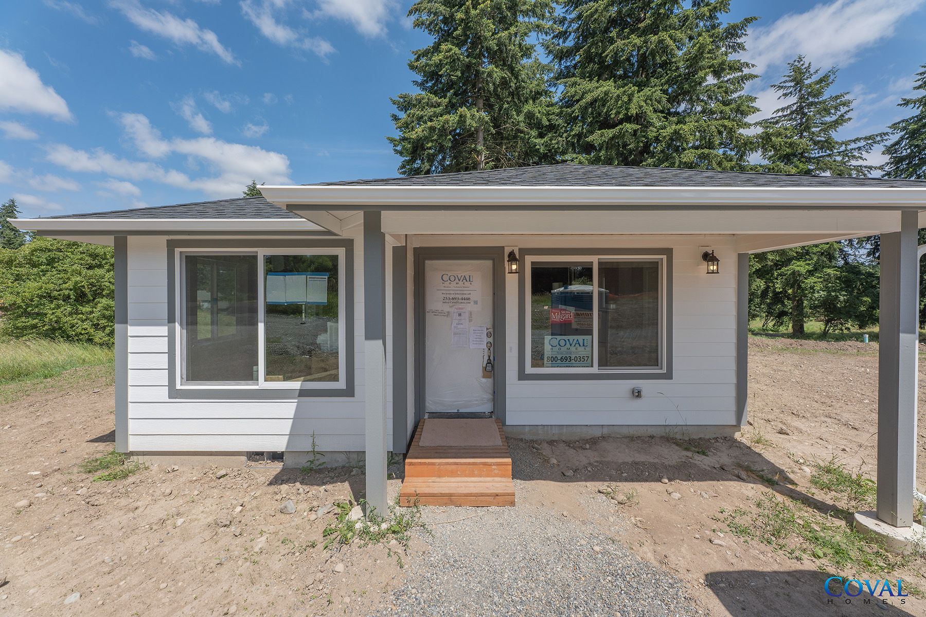 Small gray house with front porch, white trim, and gravel yard under a blue sky