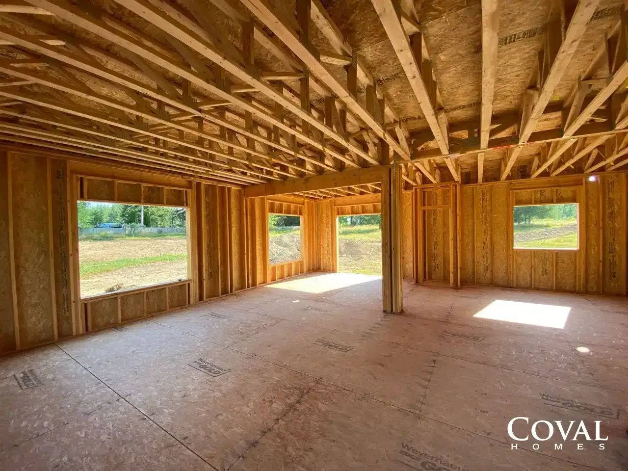 Unfinished wooden room interior with exposed beams, framed windows, and sunlight on the floor