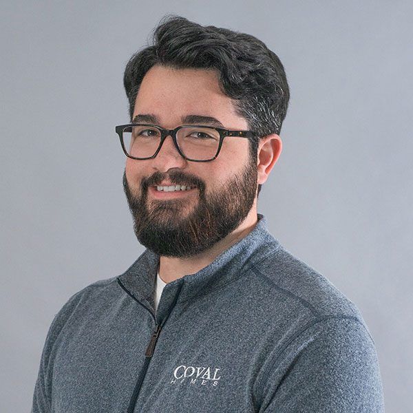 Portrait of a smiling person with glasses and a beard, wearing a gray quarter-zip sweater against a light gray background