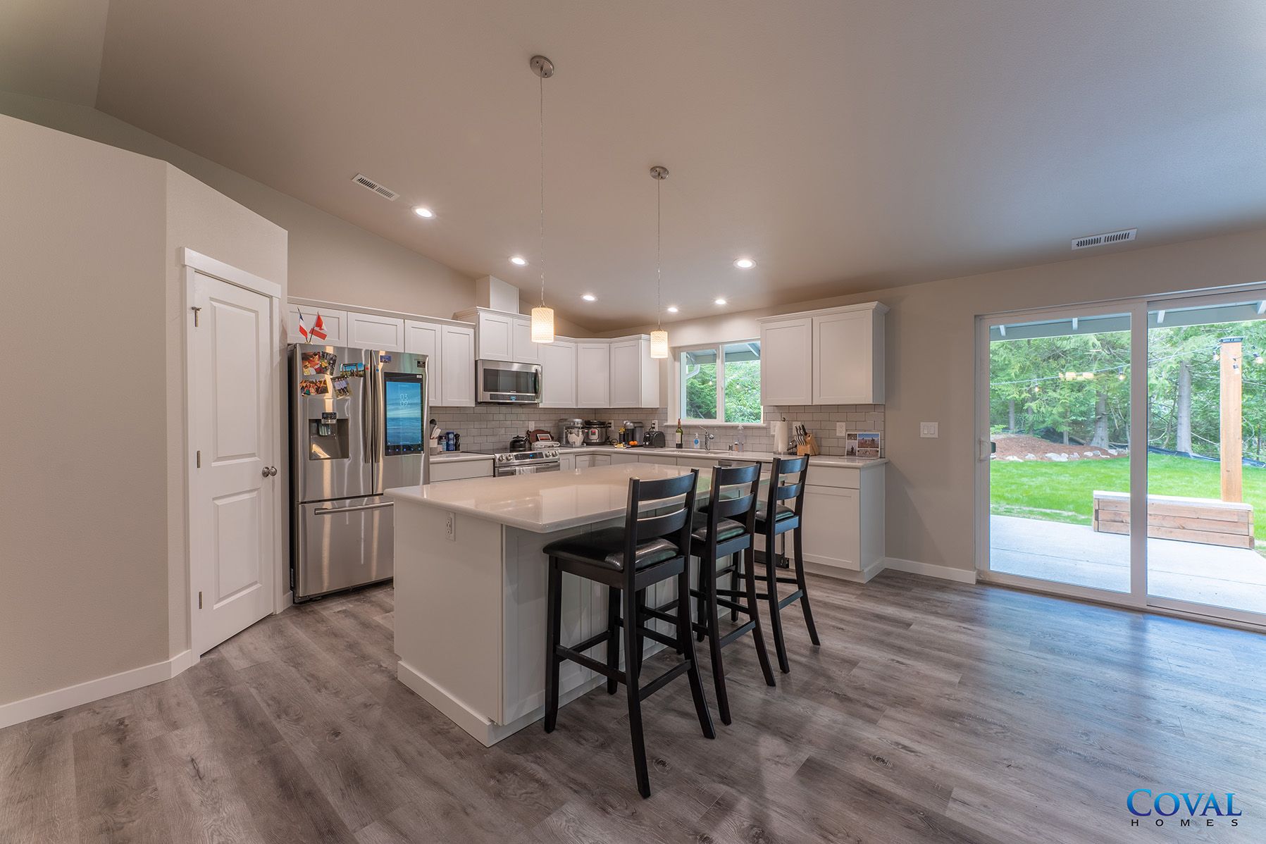 Modern kitchen with island, bar stools, stainless fridge, and sliding doors to a patio and backyard.
