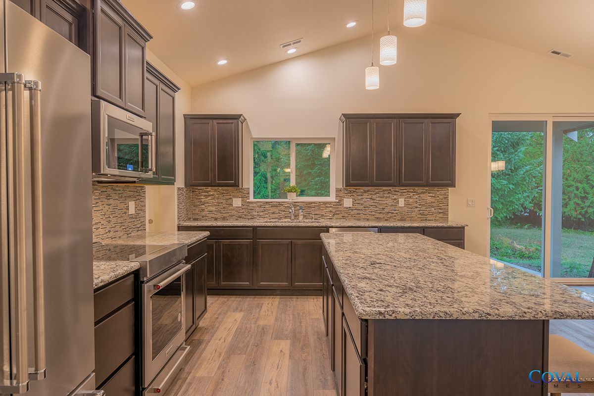 Modern kitchen with dark cabinets, granite counters, stainless appliances, and large windows overlooking greenery