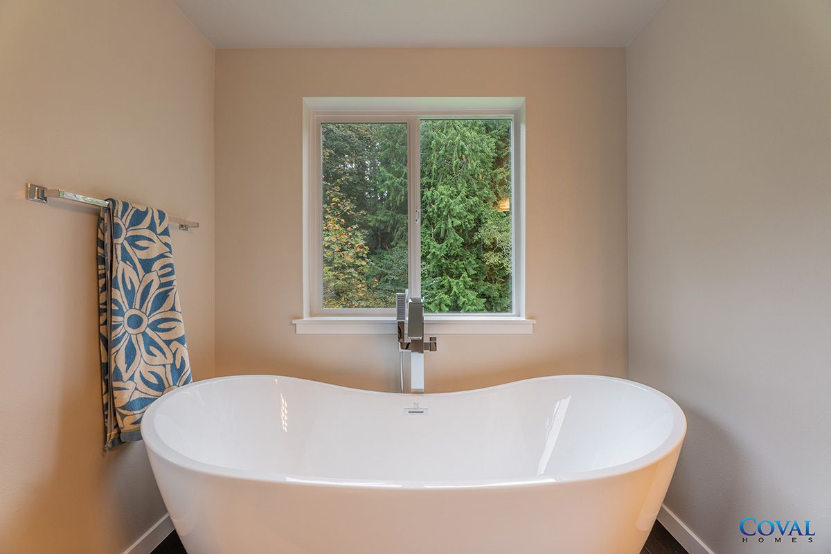 Modern bathroom with a freestanding tub beneath a window and towel rack on the left.