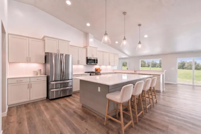 Bright white kitchen with farmhouse sink, marble countertop, and window overlooking trees.