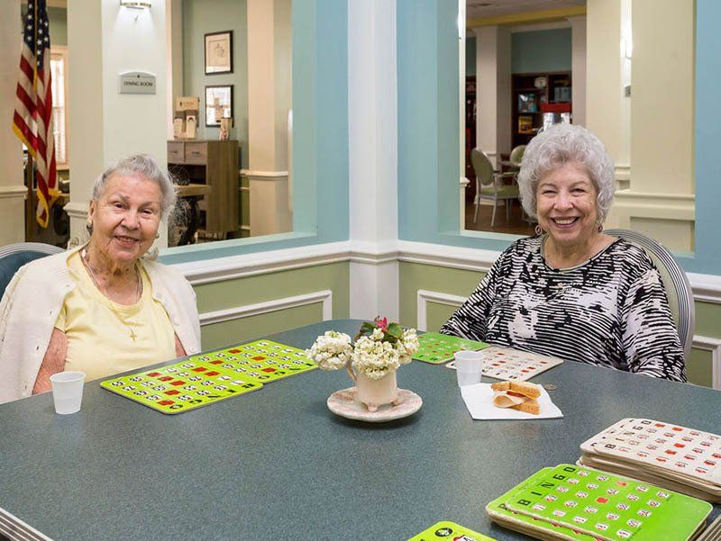 Two elderly women are sitting at a table playing bingo.
