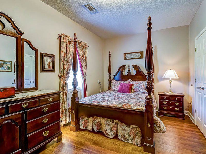 A bedroom with a four poster bed , dresser , nightstand , mirror and lamp.