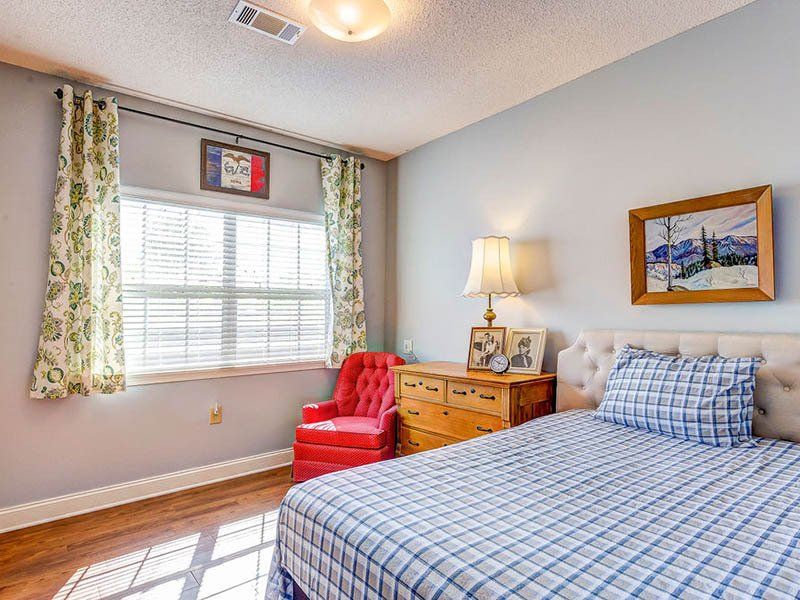 A bedroom with a bed , dresser , chair and window.