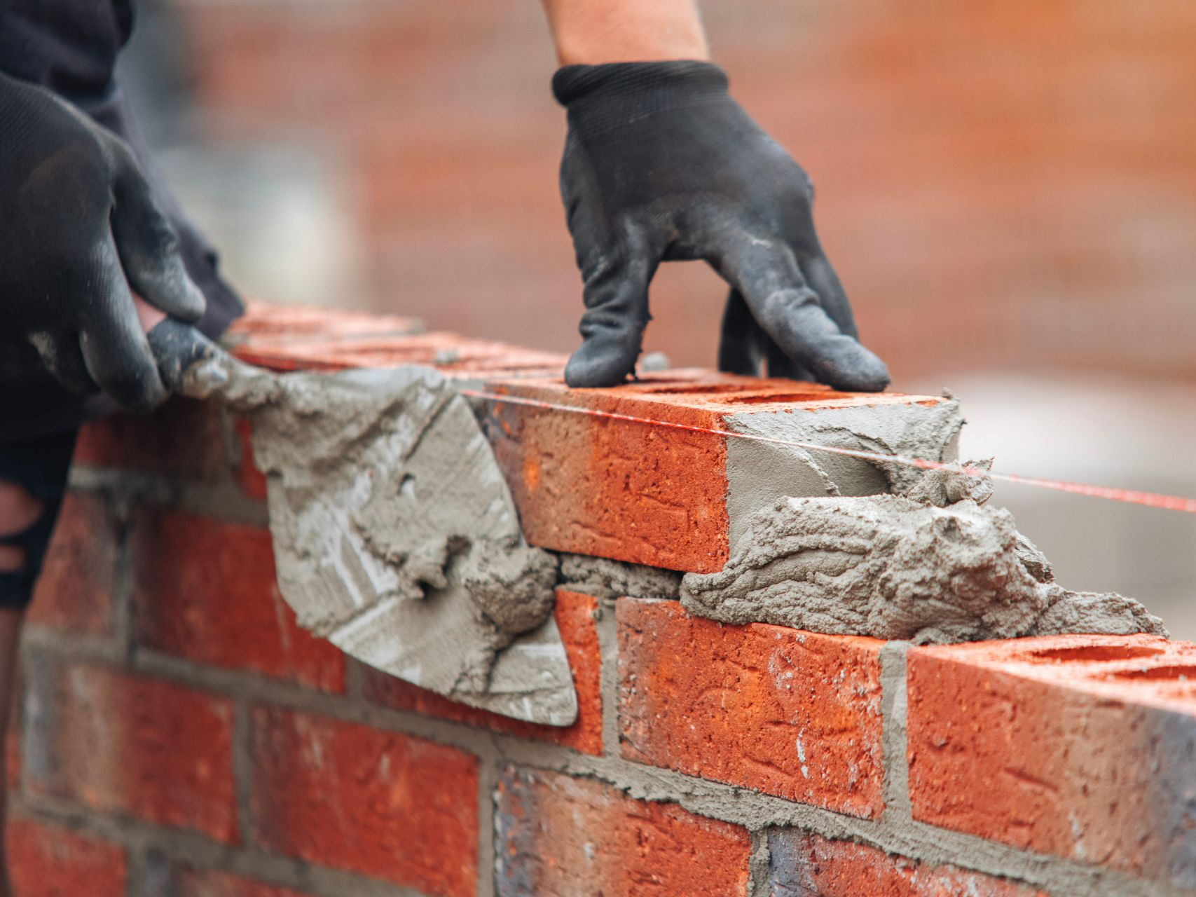 Gloved hands laying wet mortar on a brick wall during construction.